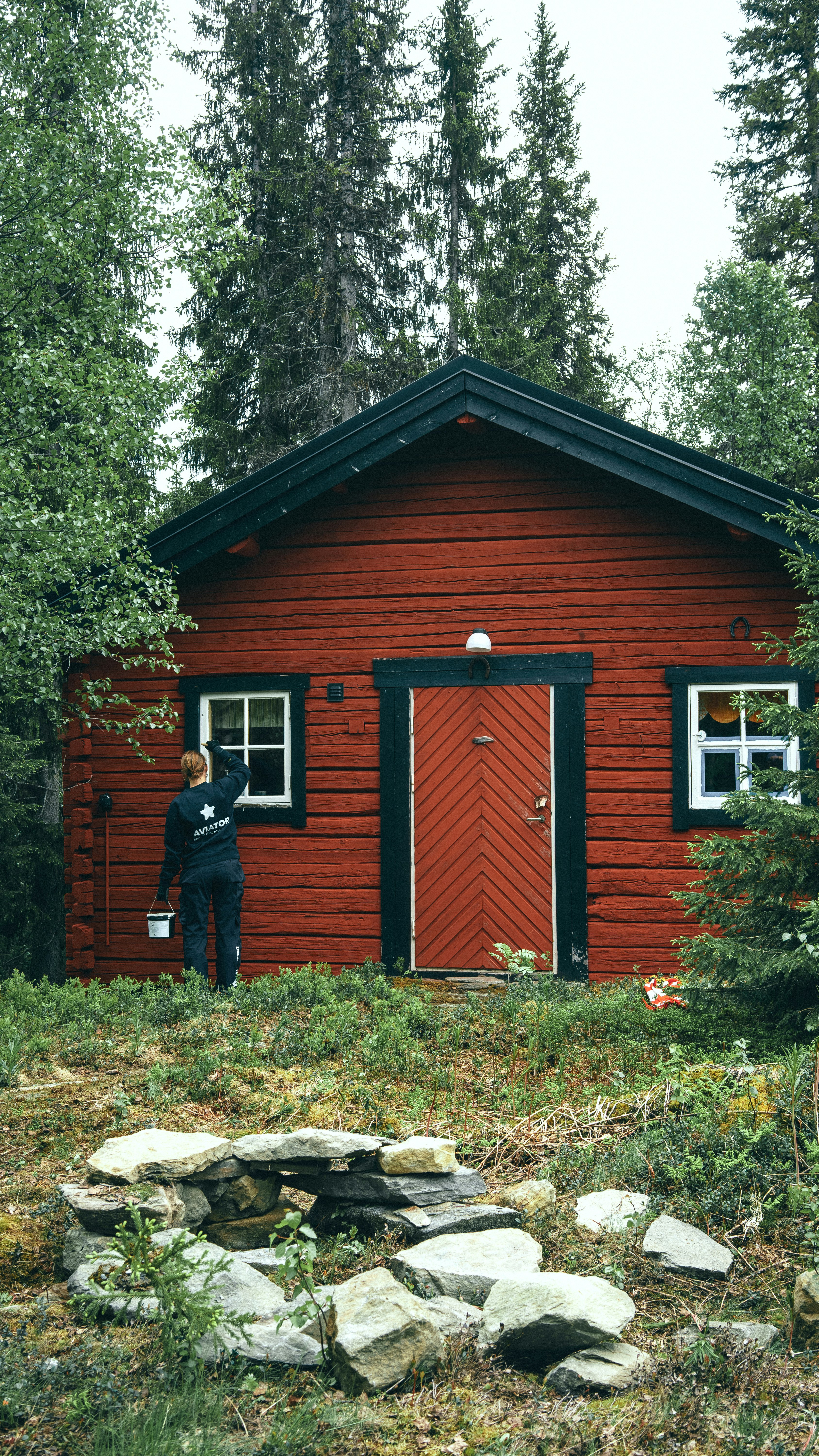 man in black jacket standing beside brown wooden house during daytime